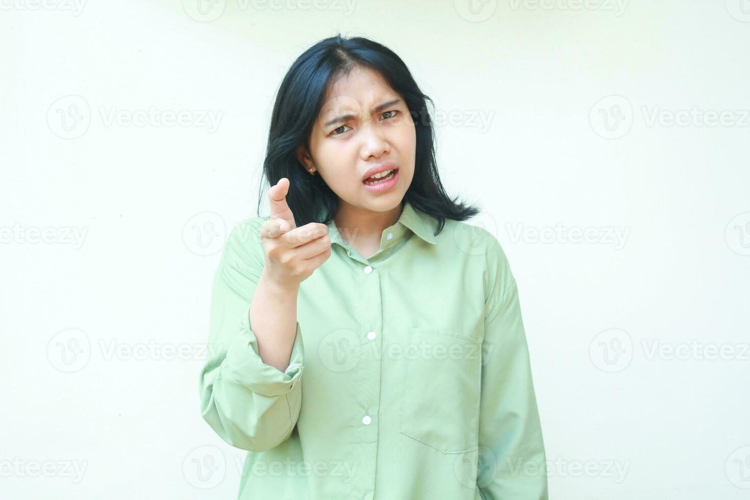angry asian woman wearing green casual clothes pointing forefinger to camera standing over isolated white background, disbelief expression, feeling annoyed and displeased photo