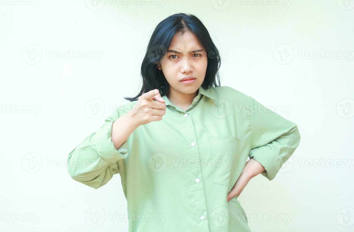 angry asian woman wearing green casual clothes pointing index finger to camera standing over isolated white background, disbelief expression, feeling annoyed and displeased gesture photo