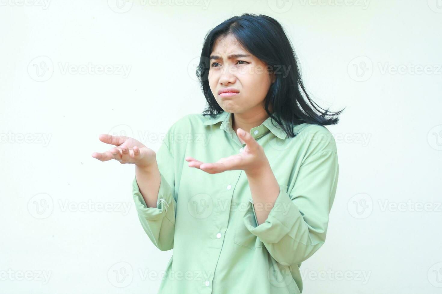 why you do that. irritated asian woman wearing green casual clothes shrugging shoulders and raising palms aside asking what happened gesture standing over isolated background, looking away photo