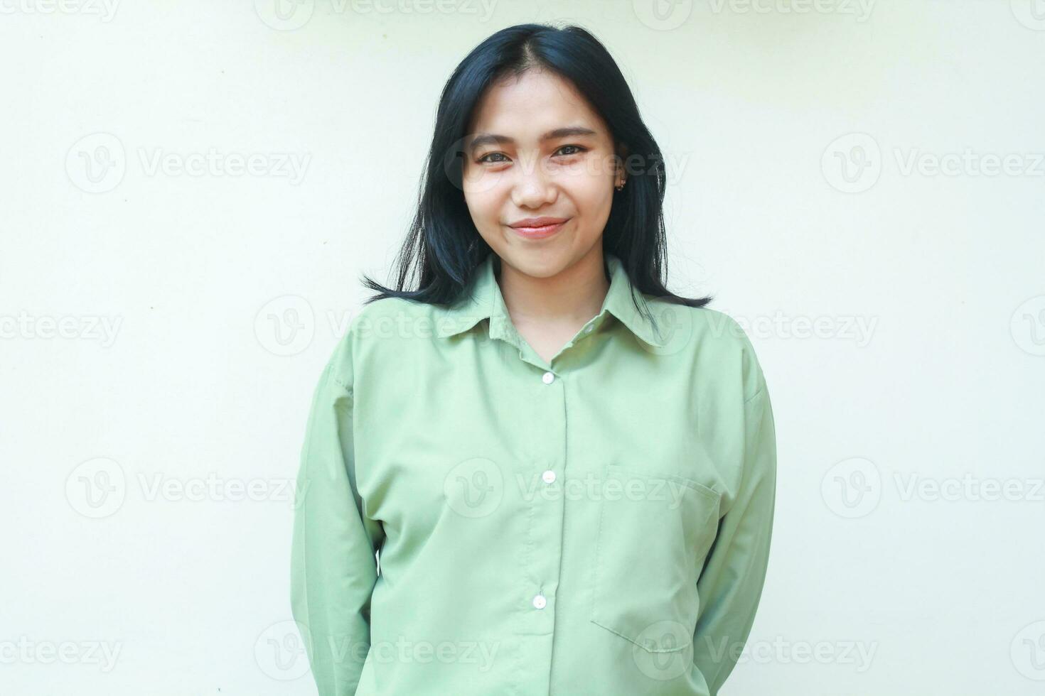 pleased confident asian woman with dark hair smiling to camera wearing green over size shirt standing over isolated background, peaceful elegant female feeling proud of her achievement photo