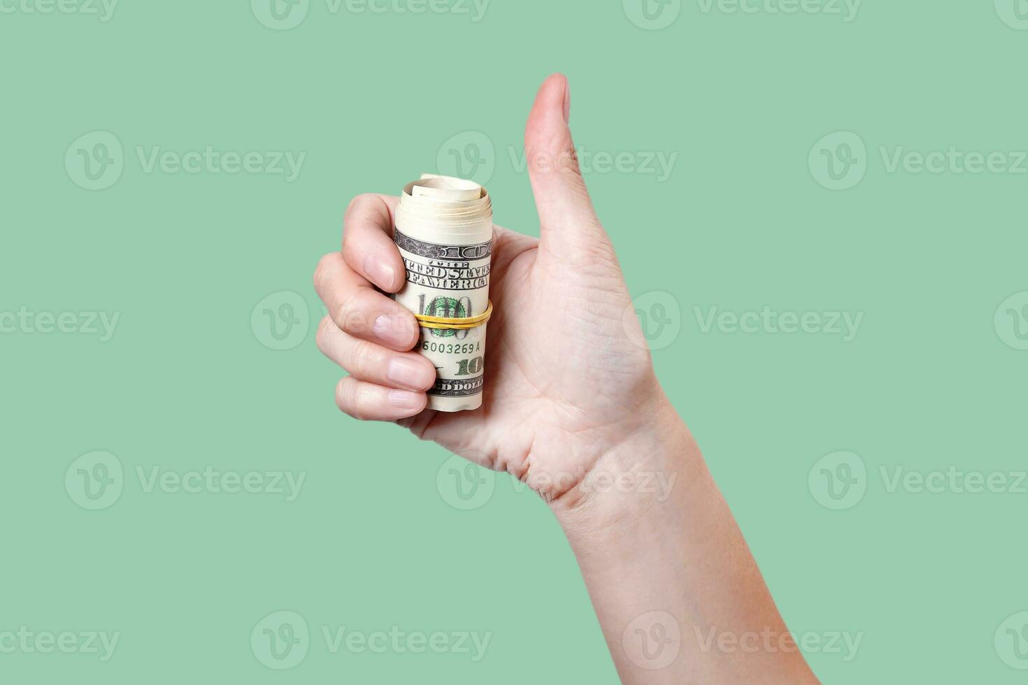 Thumbs up with roll of money isolated on green background 100 dollars photo