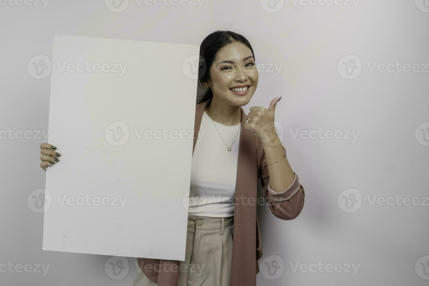 Smiling young Asian woman employee holding and showing empty blank board and gesturing thumbs up for approval, isolated by white background photo