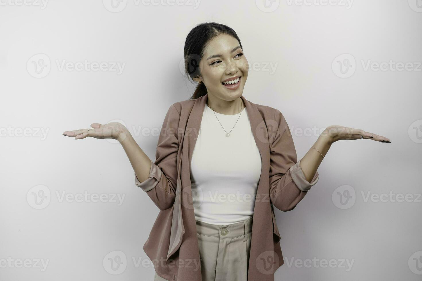 Excited Asian woman employee wearing cardigan pointing at the copy space beside her, isolated by white background photo