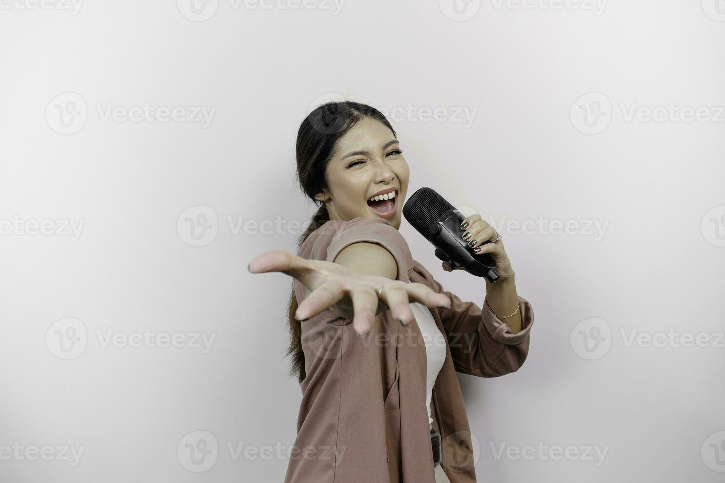 Carefree Asian woman is having fun karaoke, singing in microphone while standing over white background photo