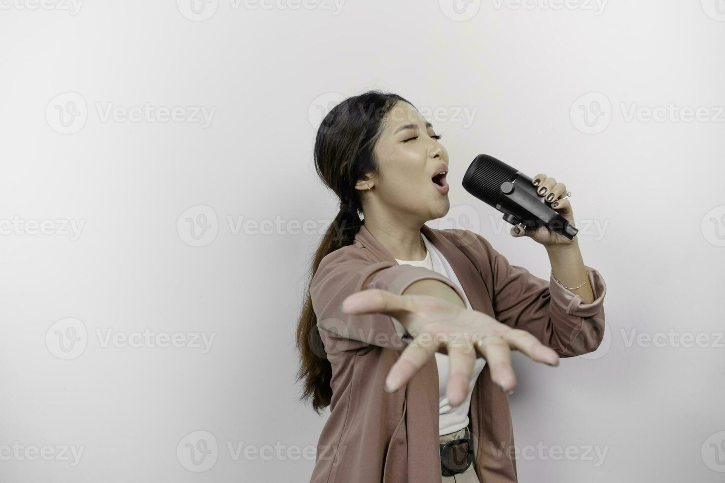 despreocupado asiático mujer es teniendo divertido karaoke, canto en micrófono mientras en pie terminado blanco antecedentes foto