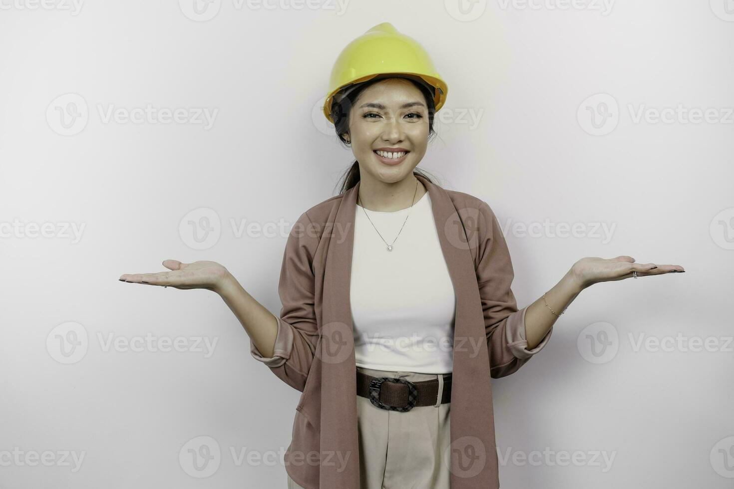 Excited Asian woman employee wearing safety helmet pointing at the copy space beside her, isolated by white background photo