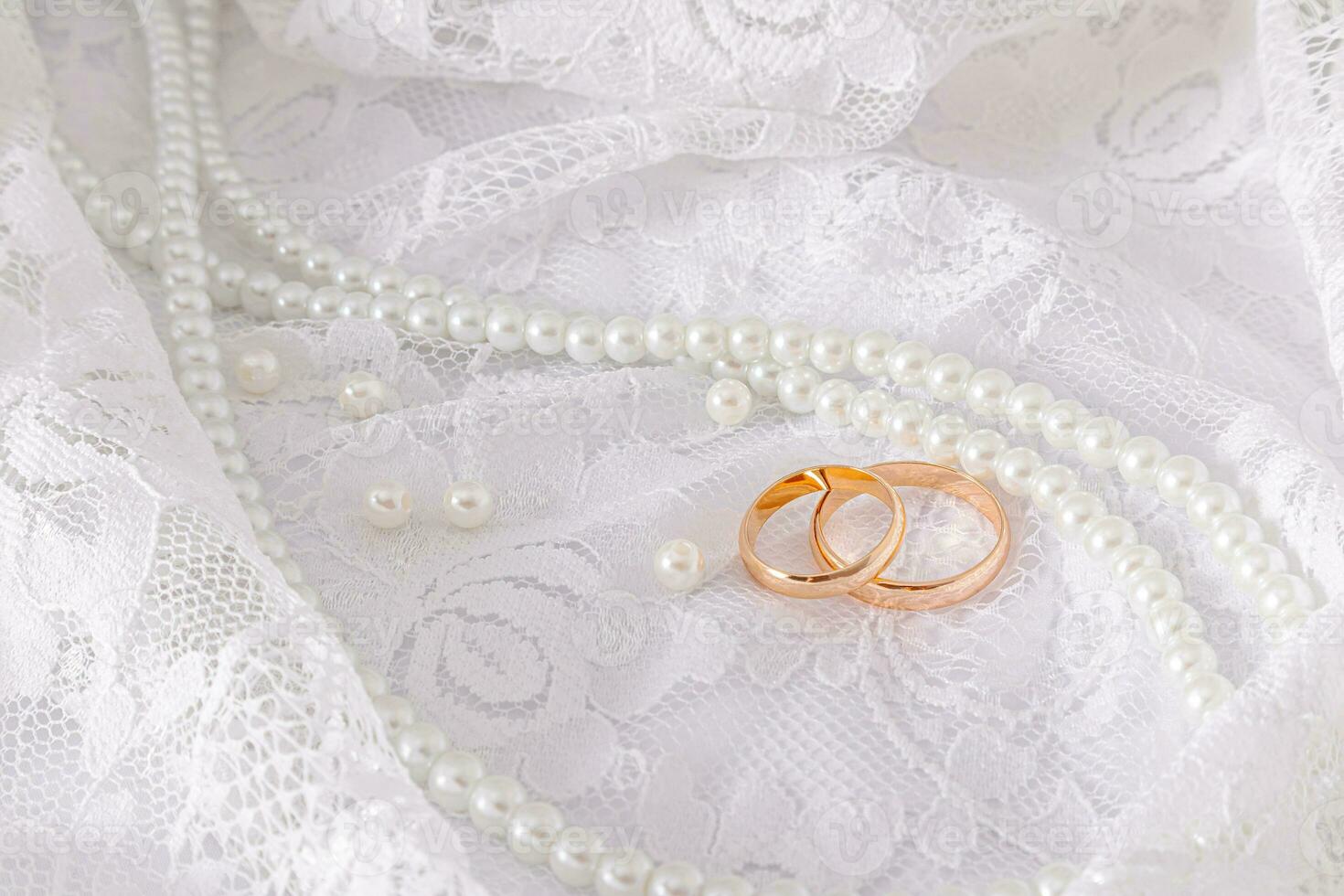 Two gold wedding rings lie on a luxurious vintage part of the bride's wedding dress with a string of pearl beads. Wedding concept. photo