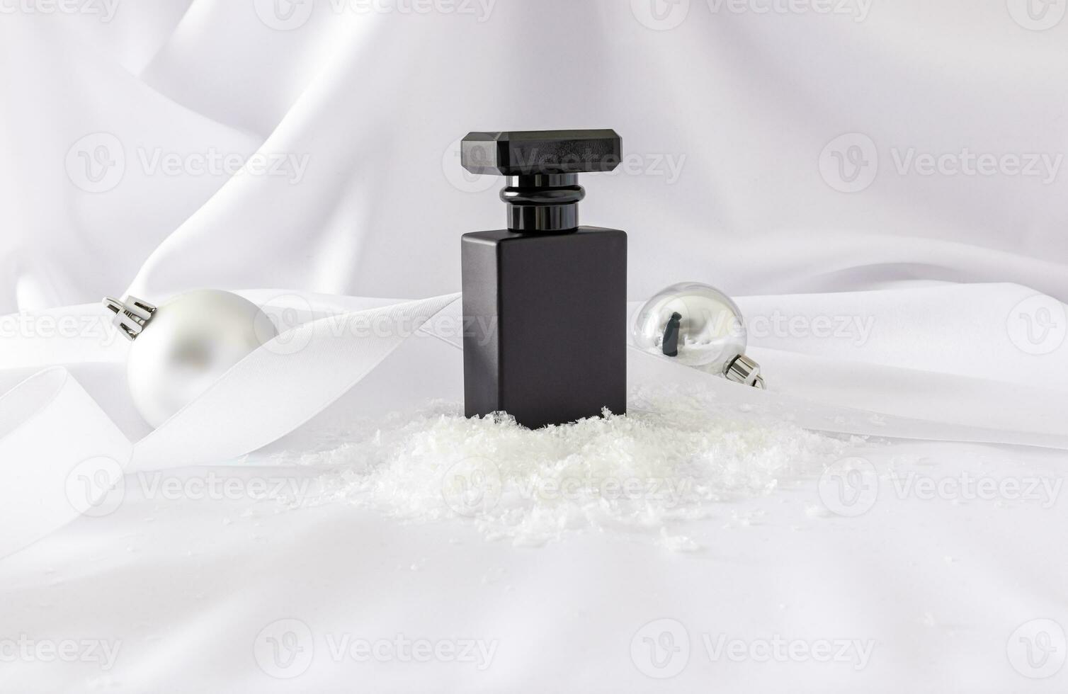 Elegant black matte bottle of cosmetic product stands on snow artificial background with silver christmas balls. New Year's perfume concept. photo