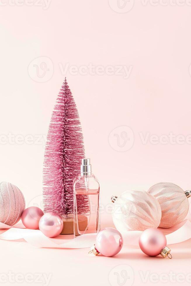 bottle of women's perfume or cosmetic spray on the background of a pink decorative Christmas tree and balloons. Vertical view. New Year's still life. photo