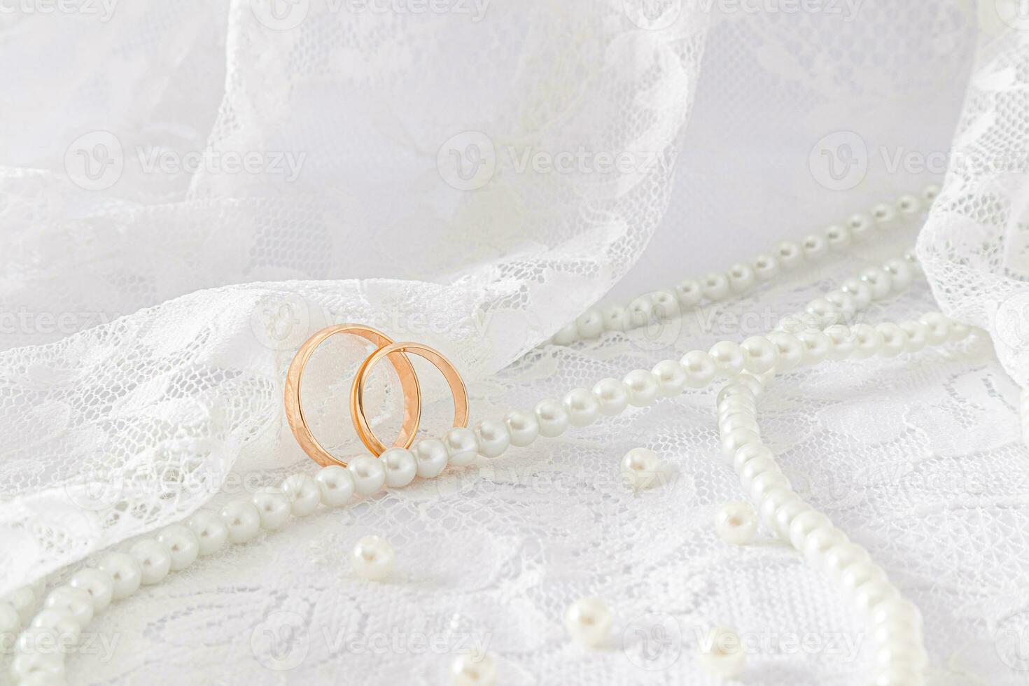 Two gold wedding rings against the soft folds of the lace fabric of the bride's dress. A long string of pearl beads. Layout for design. photo