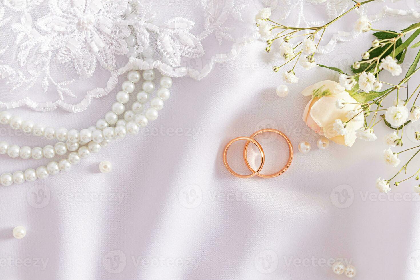 Chic wedding still life for designing a postcard, invitation, wedding cover. Two gold rings on a white satin with wedding accessories. Top view. photo