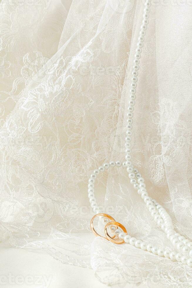 A chic wedding background for design. Antique tulle with floral ornament and a long string of pearl beads with two gold rings strung on them. photo