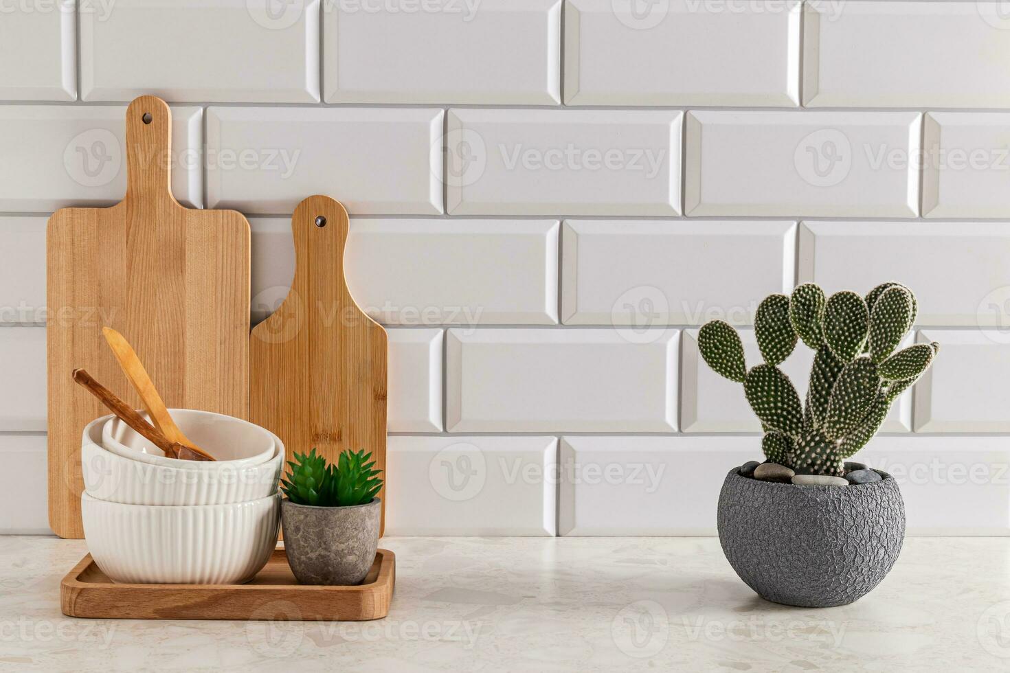 Set of ceramic bowls and cutting boards on stone light countertop in modern kitchen with potted opuntia, cactus . Front view. minimalism. photo