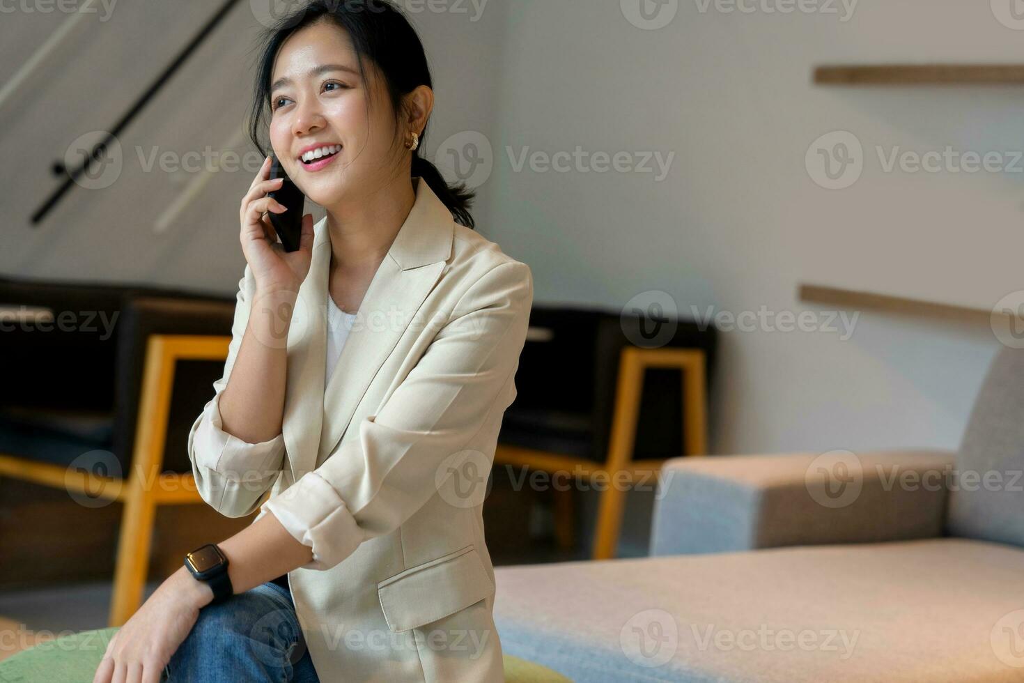 Smart freelance Asian woman sits and chats with a customer on a cell phone inside a coffee shop. with copy space photo