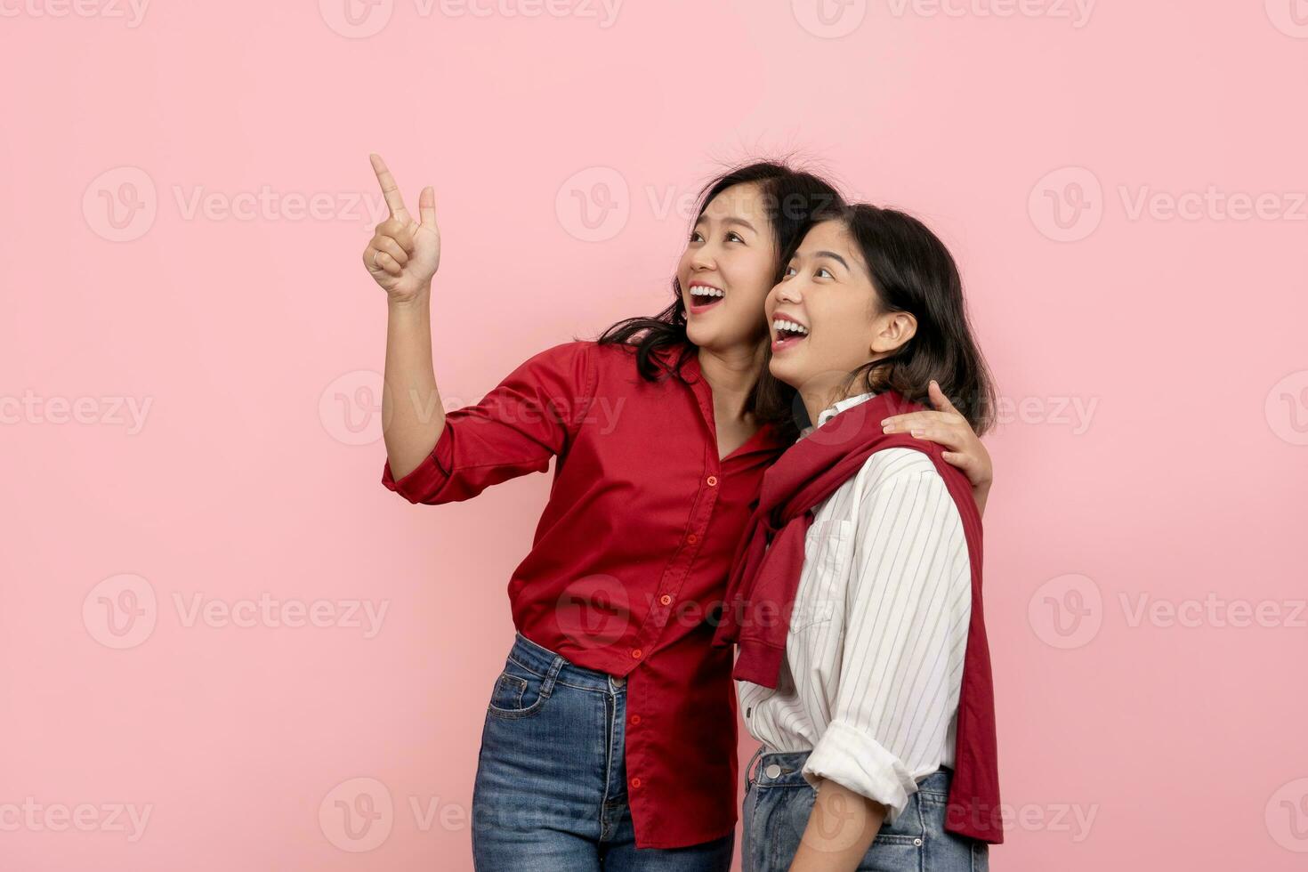 hermosa asiático mujer en rojo camisa señalando a enviar mensaje aislado atractivo y alegre asiático mujer abrazando cada otro en rosado antecedentes. foto