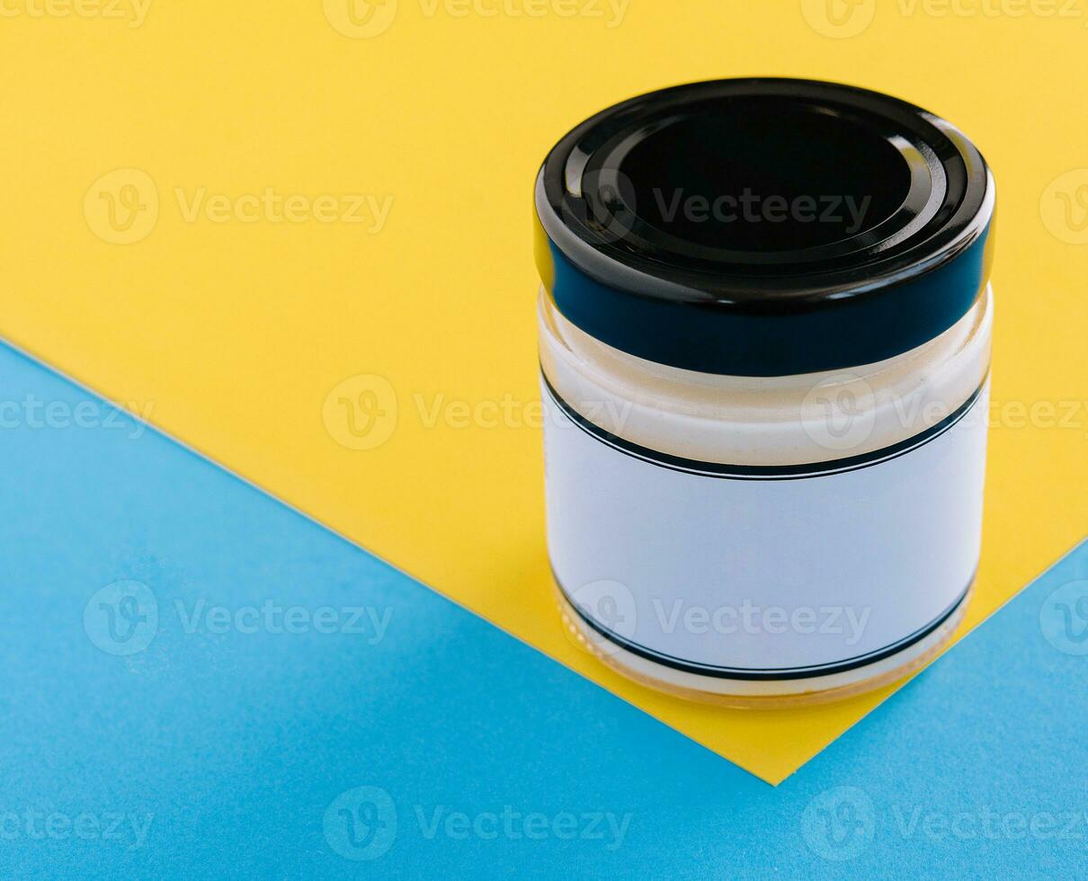 Glass mayonnaise jar with black lid on yellow photo