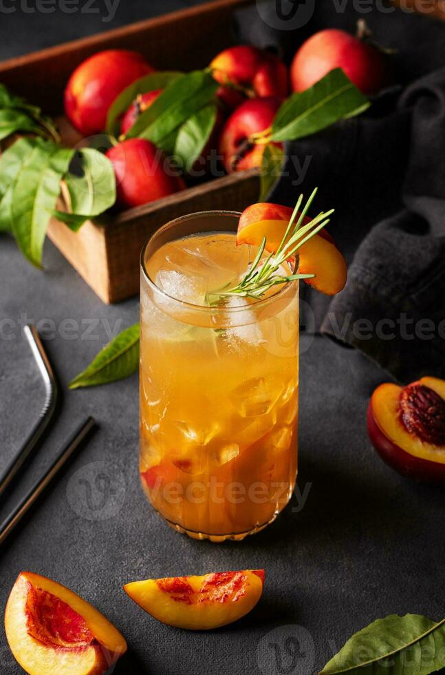Peach tea with ice and rosemary on a tall glass. Vegan homemade healthy  drink on a dark background with fresh fruits. photo