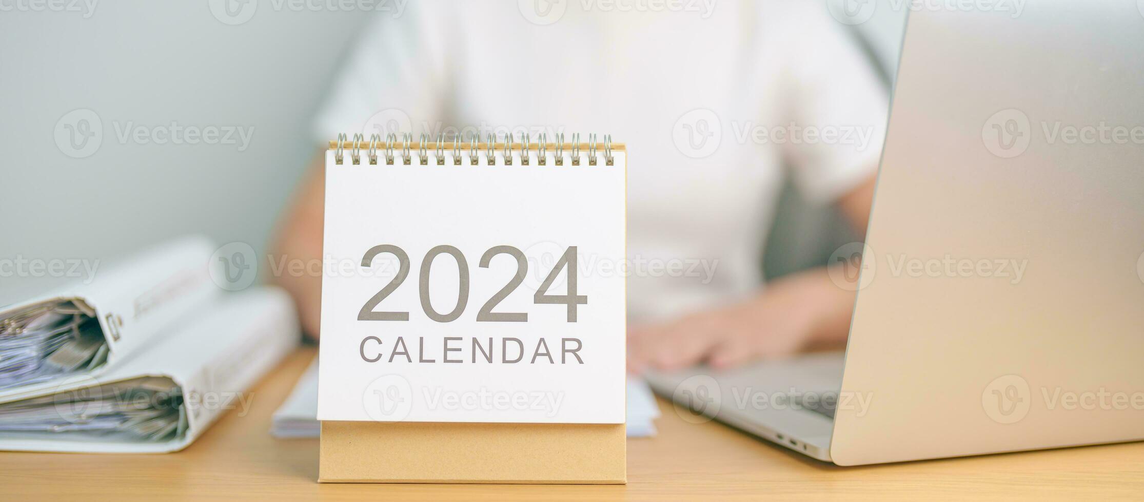 2024 Year Calendar on table with business woman using laptop computer. countdown, Happy New Year, Resolution, Goals, Plan,  Action, Mission and financial Concept photo