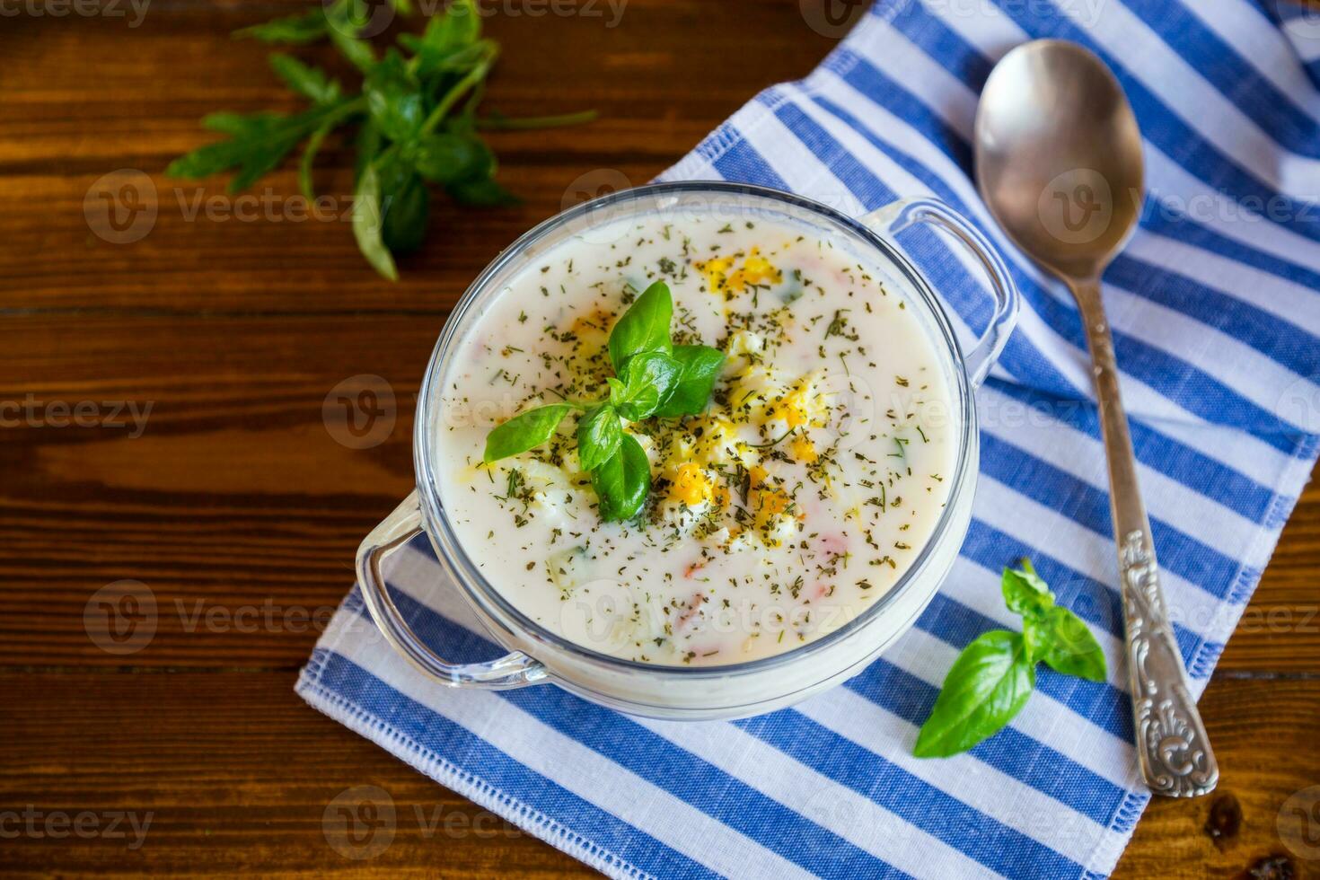 Cold soup with cucumbers, eggs, vegetables, yogurt and fresh herbs in a glass bowl . photo