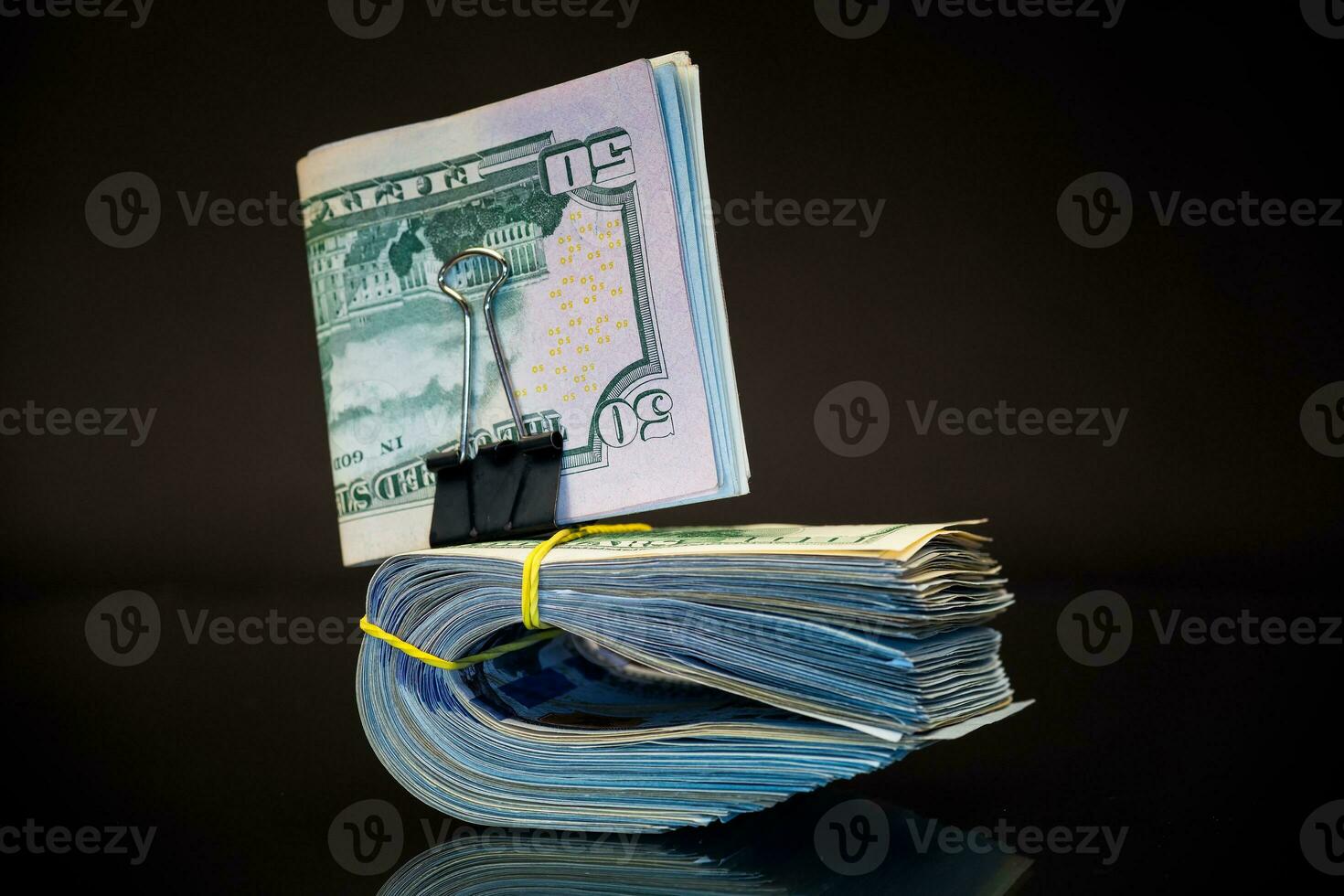 stack of dollar bills collected in an elastic band and a stationery clip photo