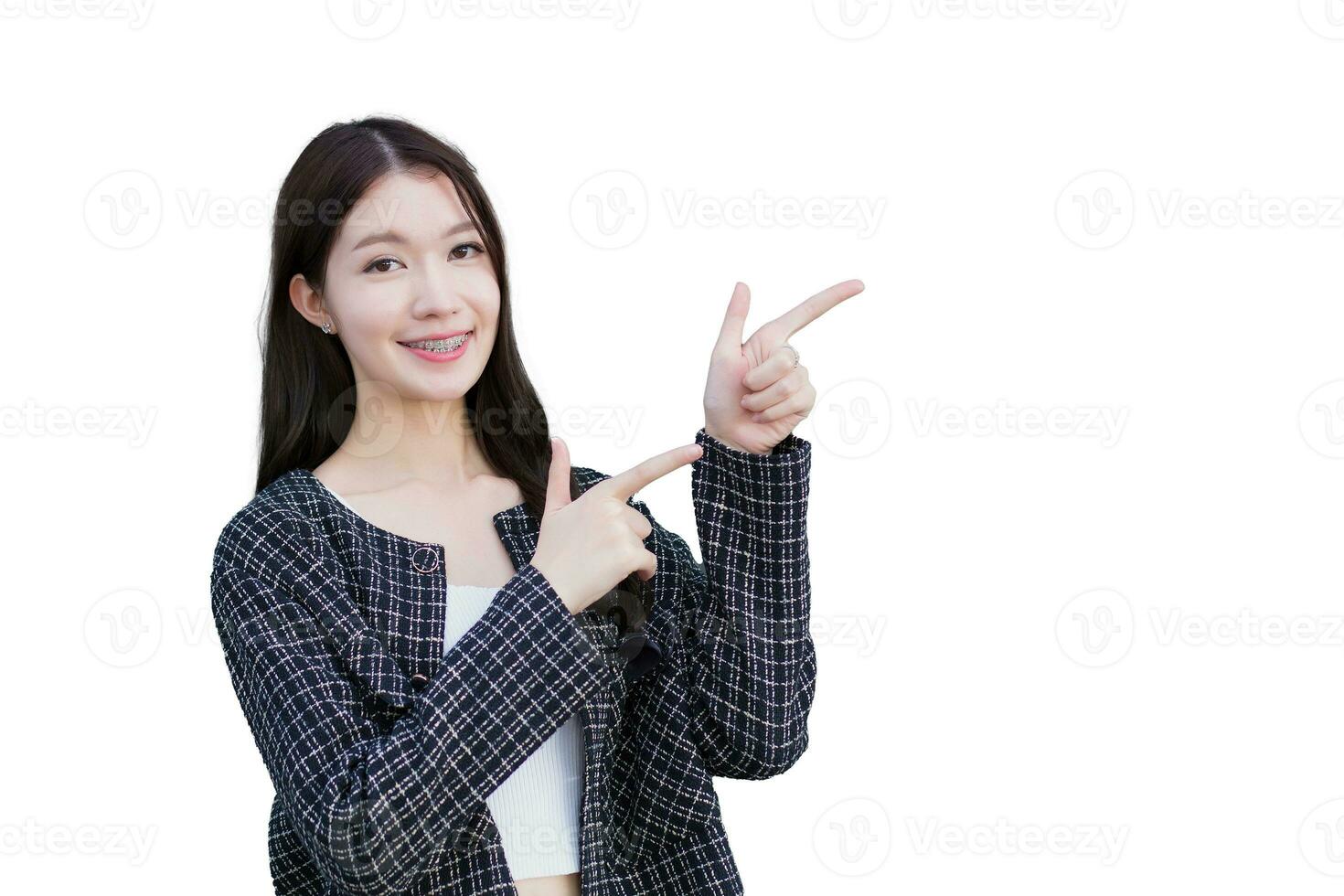 Professional Asian working woman who wears black suit with braces on teeth is pointing hand to present something while isolated on white background. photo
