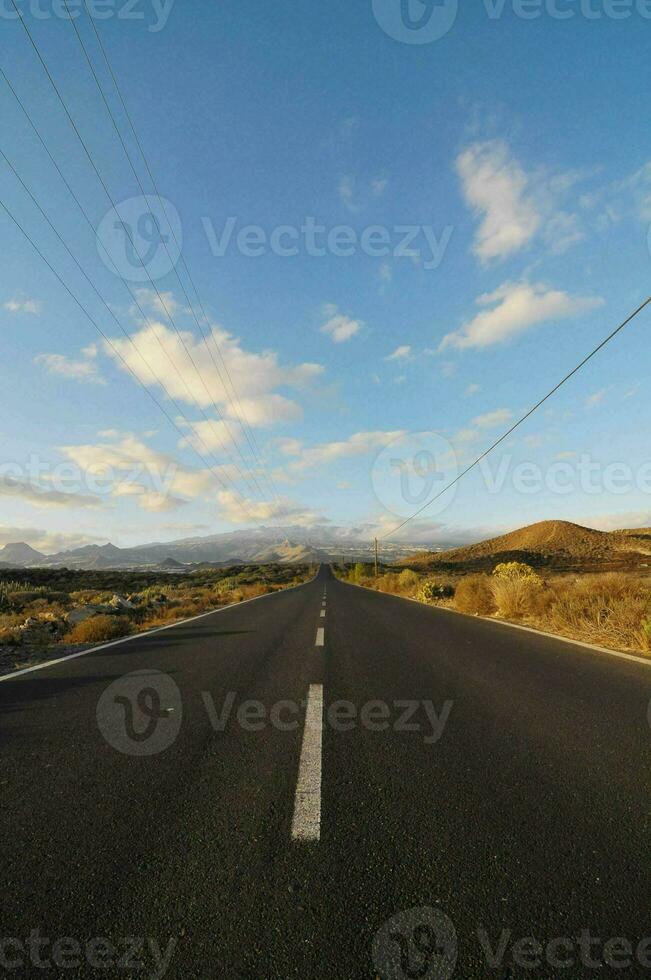an empty road with power lines and mountains in the background photo