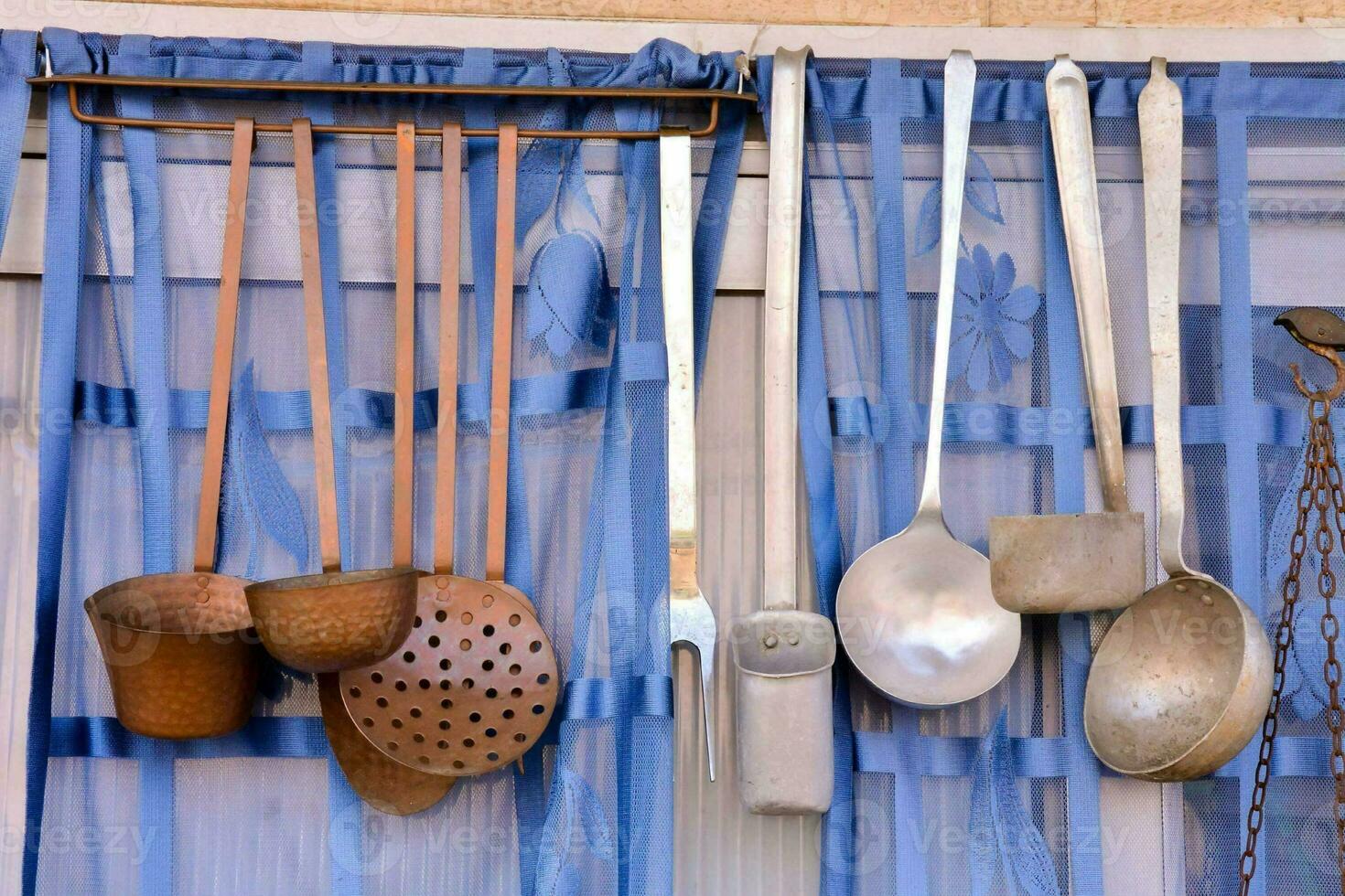 a collection of kitchen utensils hanging from a blue curtain photo