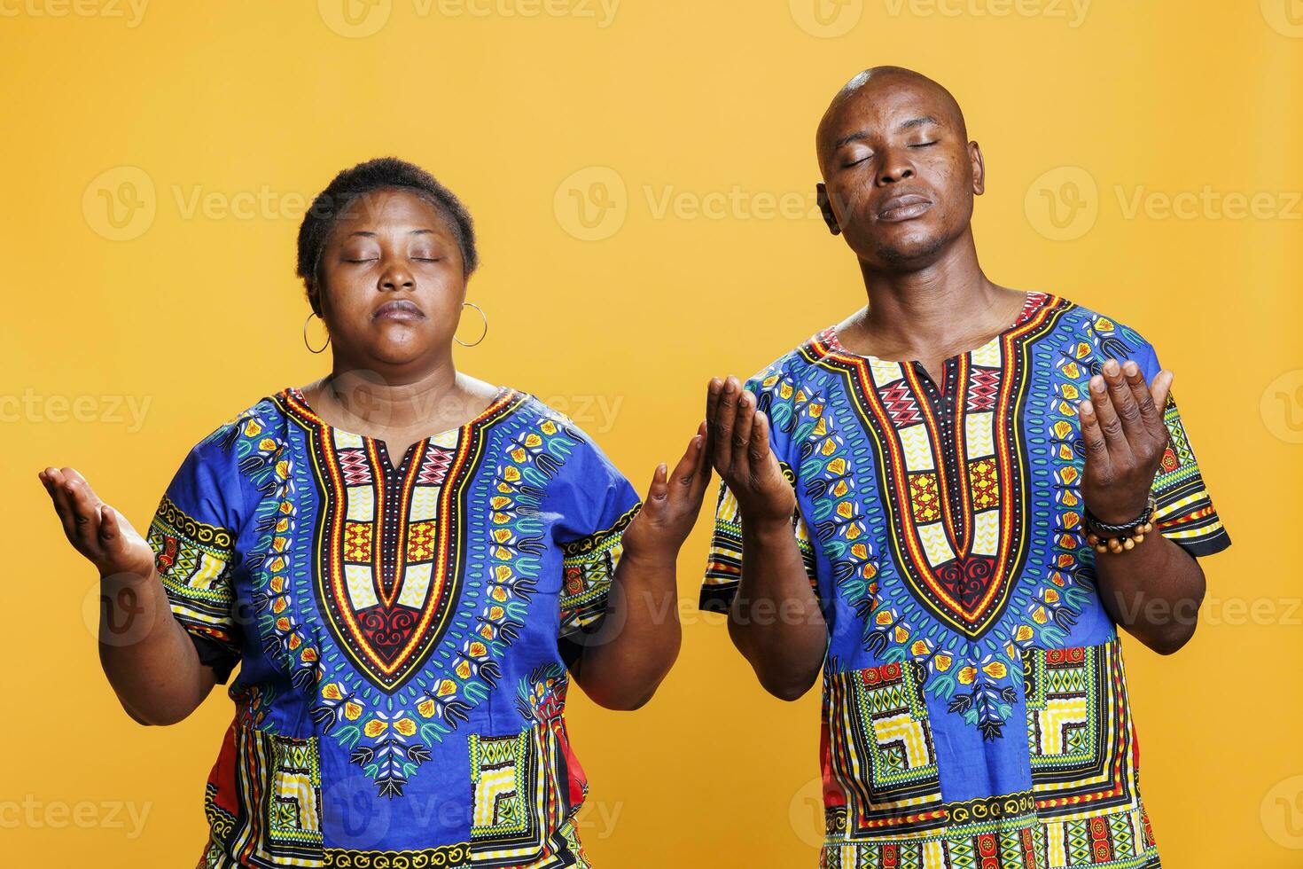 Religious man and woman black couple wearing ethnic clothes praying and standing palms wide open. Prayers with closed eyes posing with spread arms while asking god for blessing photo