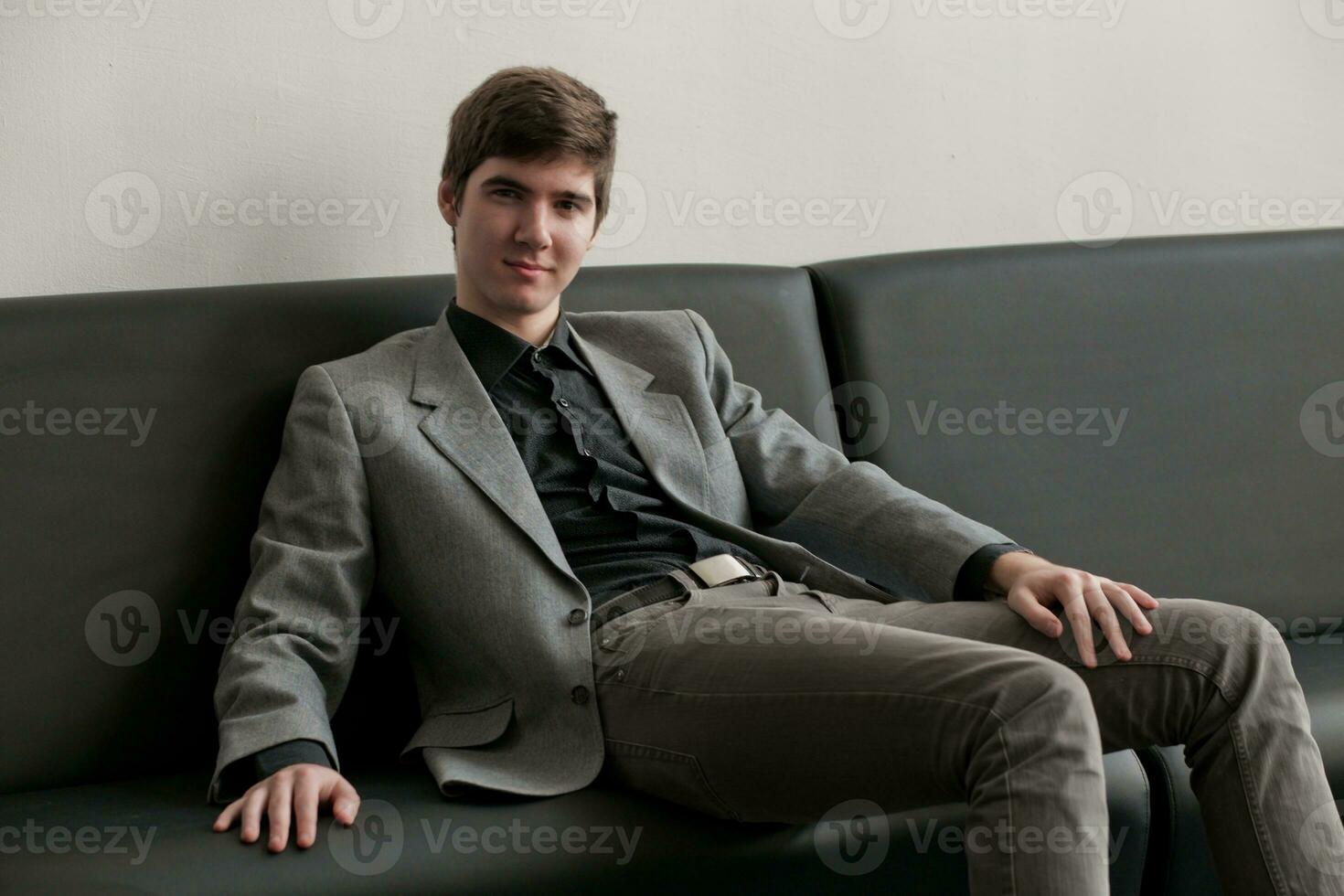 hermoso joven hombre en traje sentado en sofá en recepción. negocio hombre esperando para reunión. foto