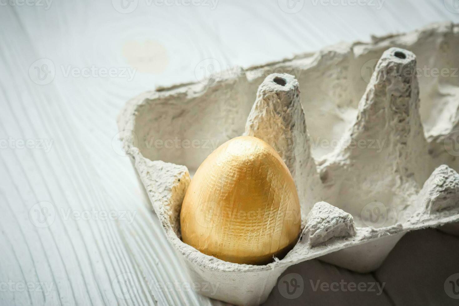 Golden egg in a regular cardboard egg tray. The concept of a rich life. photo