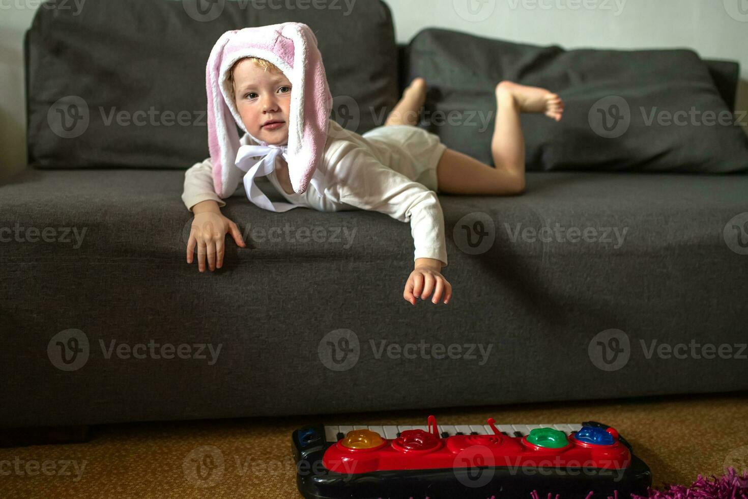 A little funny girl in a hat with hare ears lying on the couch. The child plays role-playing games at home. photo