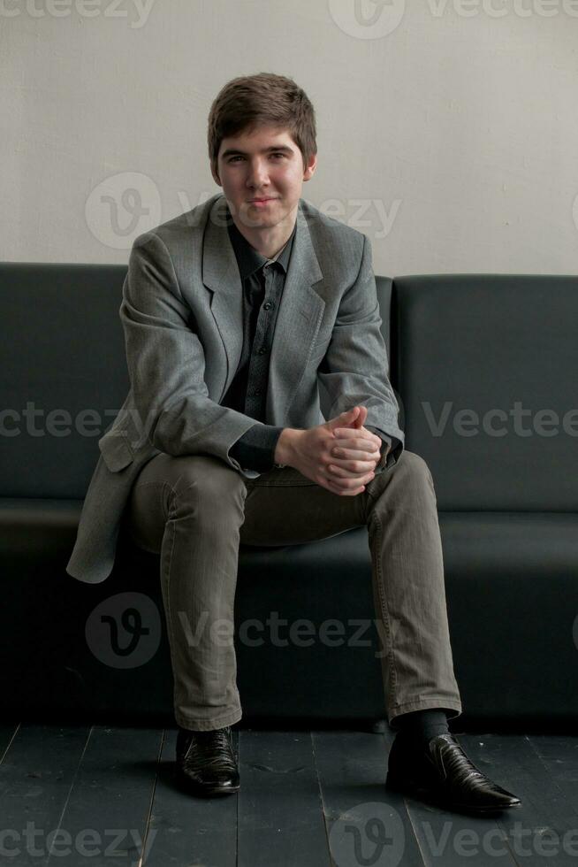 Handsome young man in suit sitting on couch in reception. Business man waiting for meeting. photo