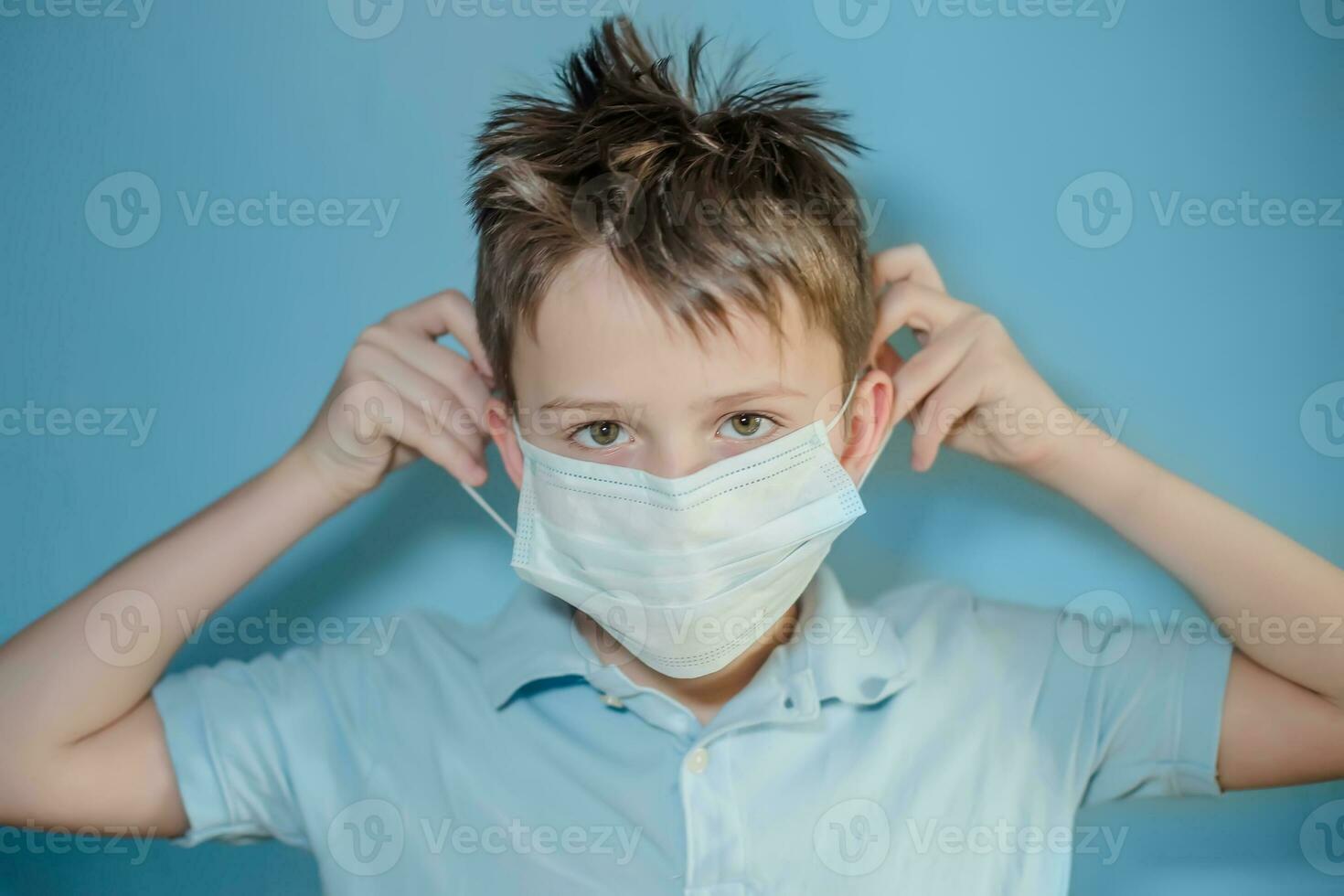 boy puts on a medical protective mask on blue background. child with flu, influenza or cold protected from viruses, pollution in bad epidemic situation, among patients with coronavirus photo