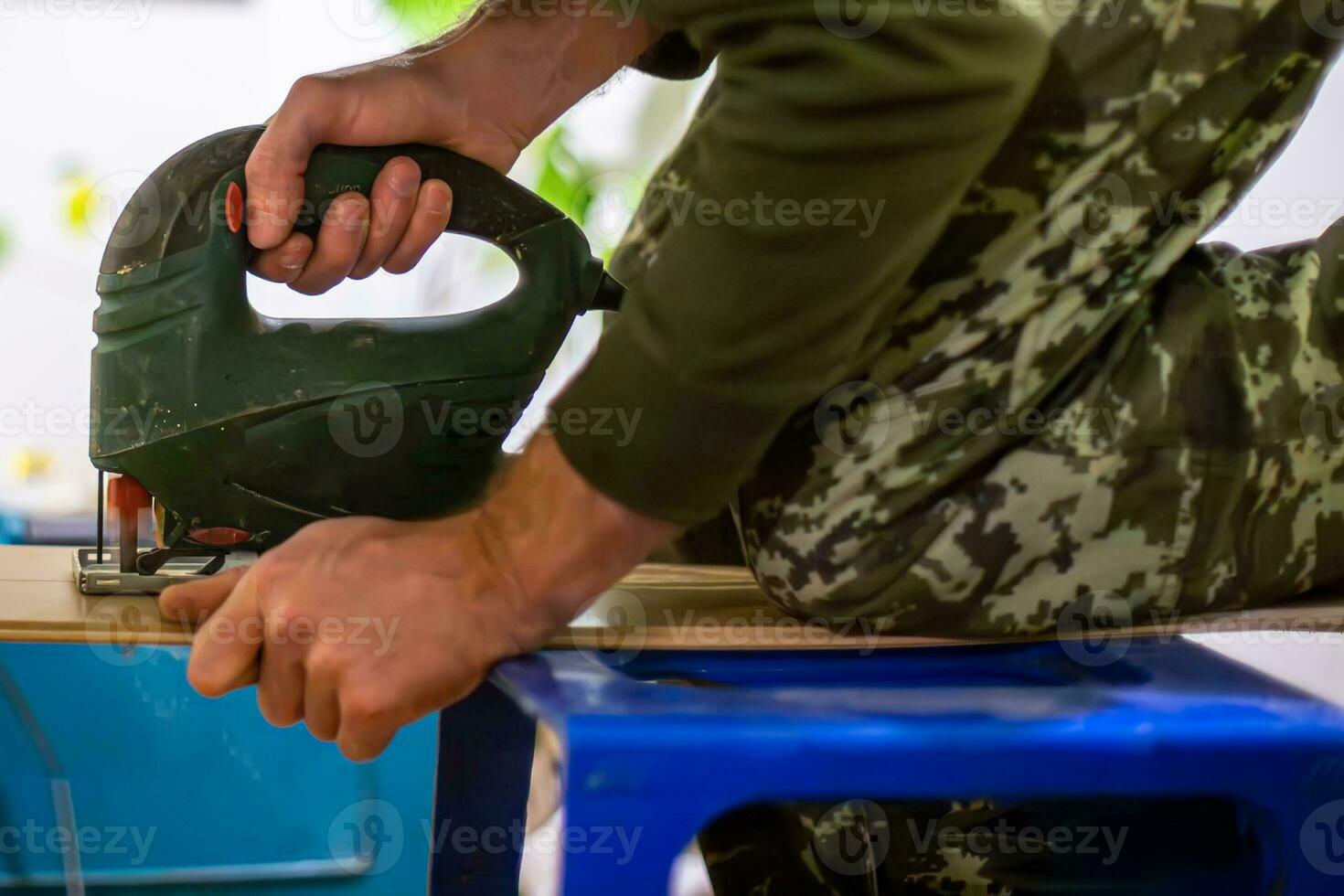 carpenter using an electric jigsaw to repair a piece of furniture. The carpenter is using the jigsaw to replace a damaged piece of wood, and the furniture is restored to its former glory. photo