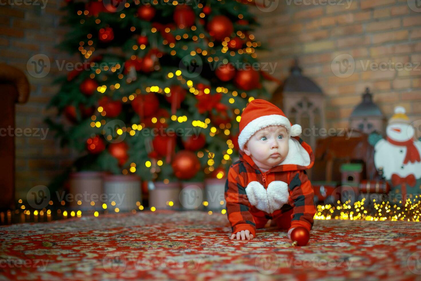 Little surprised child in santa costume in festive room on Christmas eve. Girl on background of Christmas tree. photo