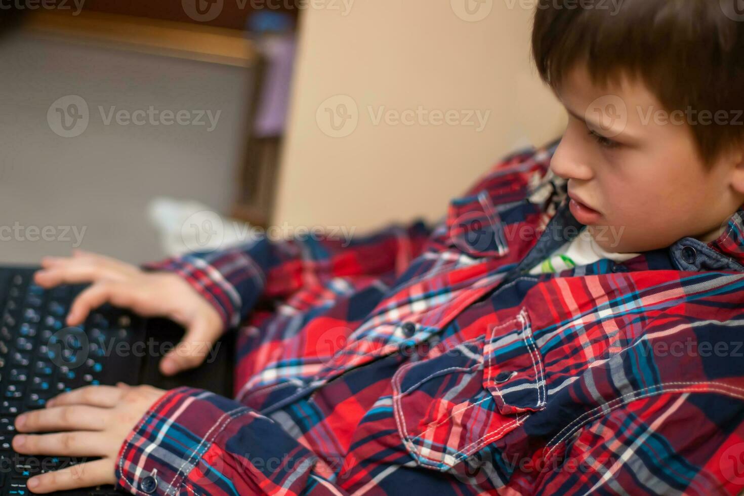 boy in plaid shirt does lessons on laptop. child learns remotely during quarantine of coronavirus. Online learning from home. photo