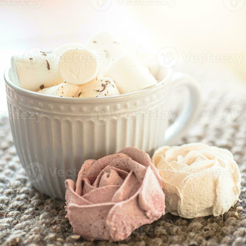 A cup of cocoa or chocolate next to a rose-shaped marshmallow. Warm cozy square background. photo