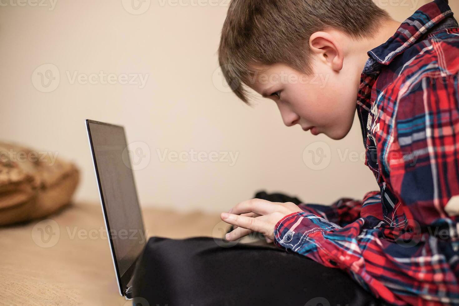 boy in plaid shirt does lessons on laptop. child learns remotely during quarantine of coronavirus. Online learning from home. photo