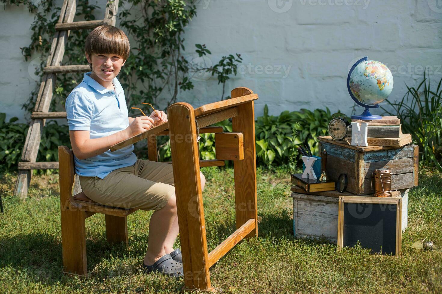 schoolboy sits at desk in street. Preparing for school. boy holds glasses. Back to school concept photo