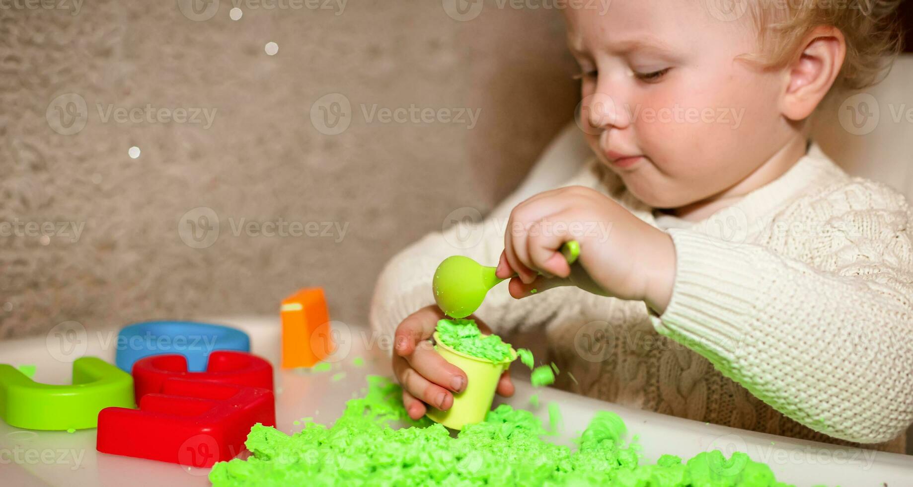 baby holds mold for playing with sand at home. Educational toys for children up to year. girl plays with kinetic sand. child builds shepherds in form of letters of sand. Early development of children. photo