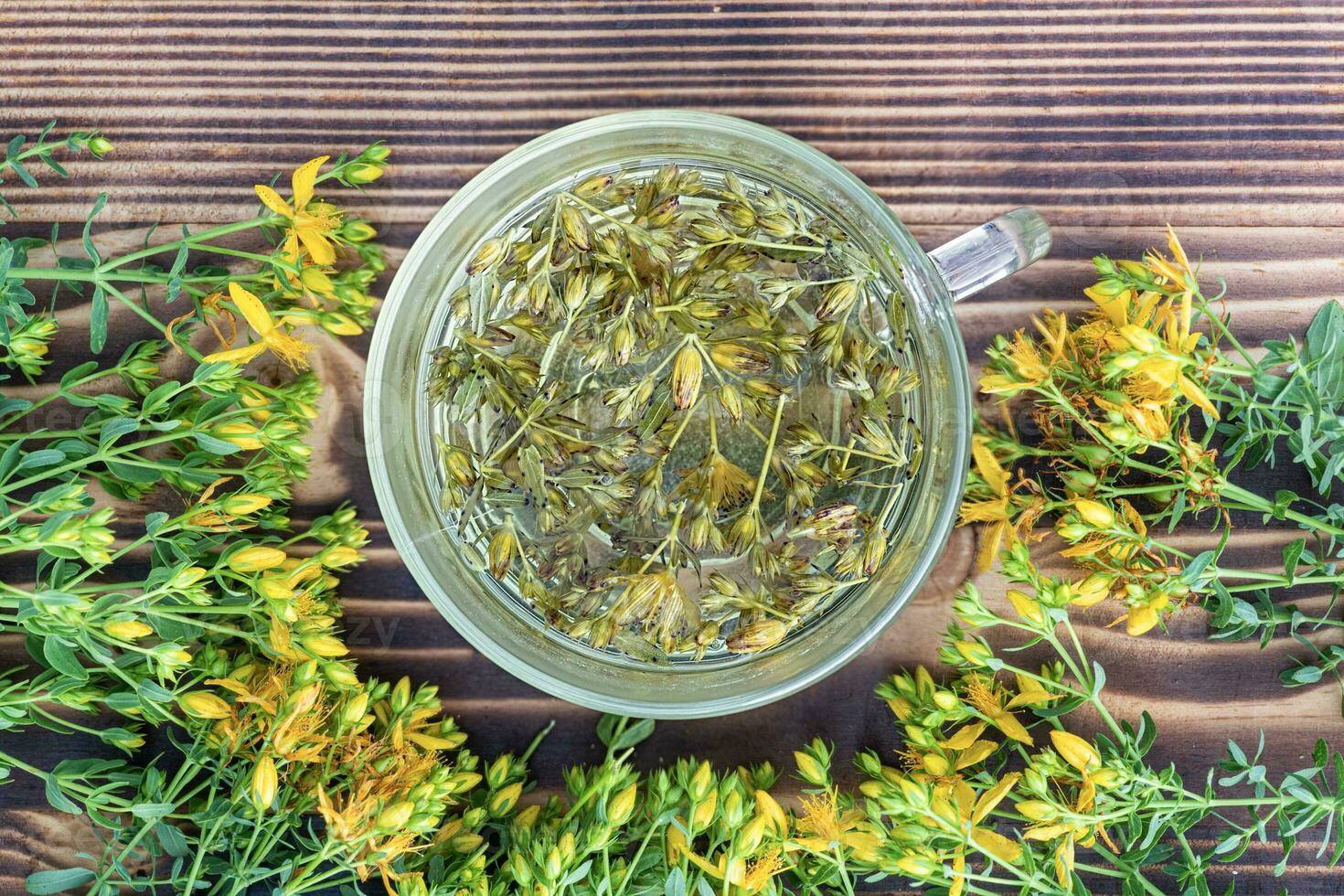 Hypericum - St Johns wort plants yellow flower used in alternative medicine. Herbal tea in transparent cup. Useful homeopathic elexir on wooden table photo