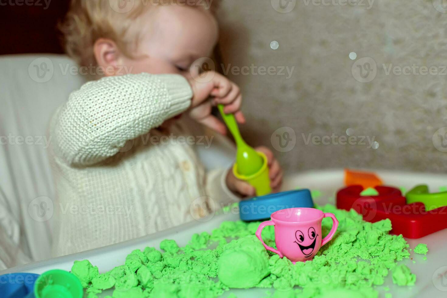 baby holds mold for playing with sand at home. Educational toys for children up to year. girl plays with kinetic sand. child builds shepherds in form of letters of sand. Early development of children. photo