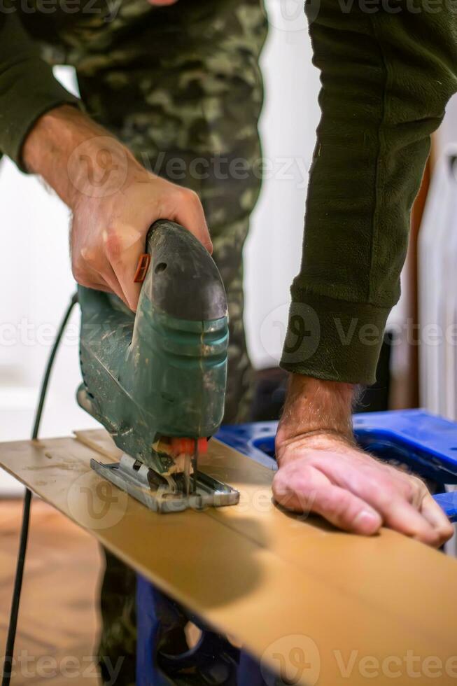 An electric jigsaw in the hands of a man. Carpenter cutting wooden plywood to make furniture photo