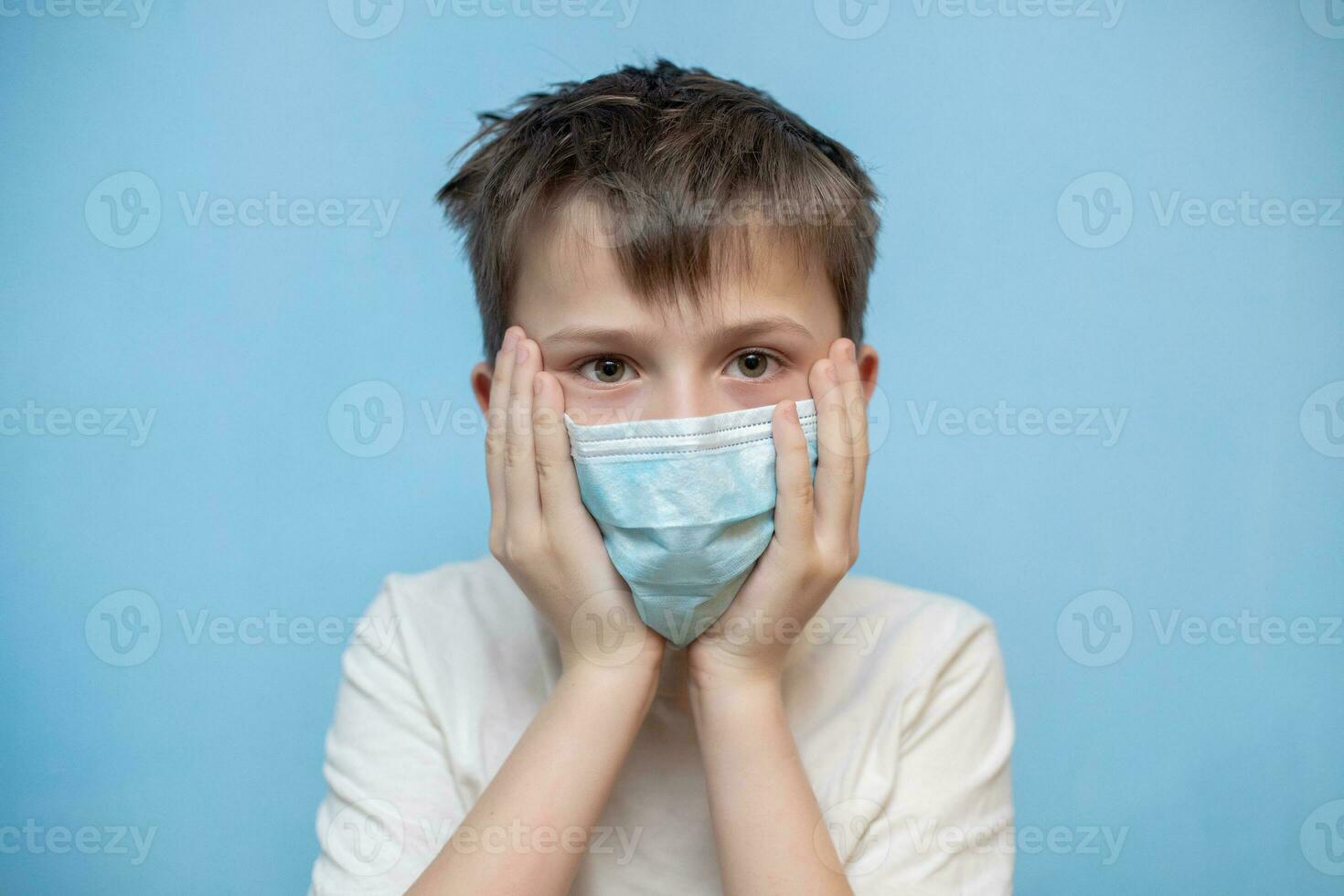 terrified boy in medical protective mask grabbed face with hands. hild with flu, influenza or cold protected from viruses, in bad epidemic situation, among patients with coronavirus photo