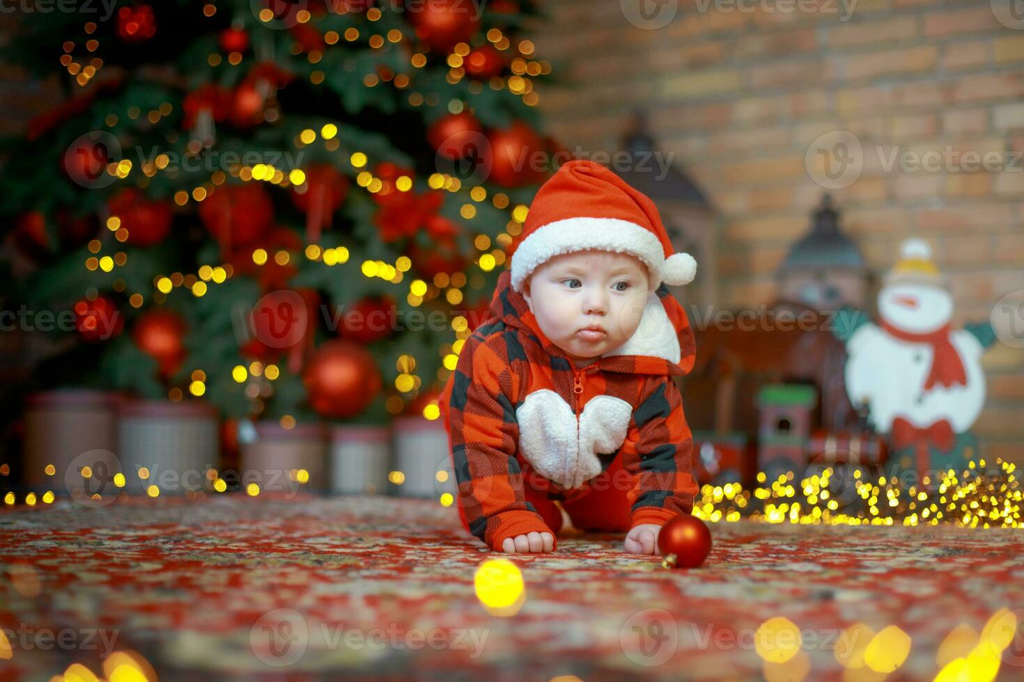 Little happy girl of 6 months creeps near a New Year tree on Christmas Eve. child in Santa Claus costume near luminous garlands. Happy new year 2020 concept photo