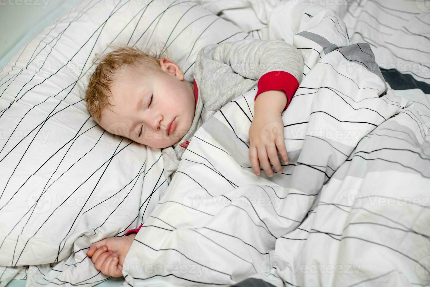 little child sleeps in bed in protective medical mask. sick child in white bed. Kid toddler one years old with flu, influenza or cold protected from viruses, pollution among patients with coronavirus photo