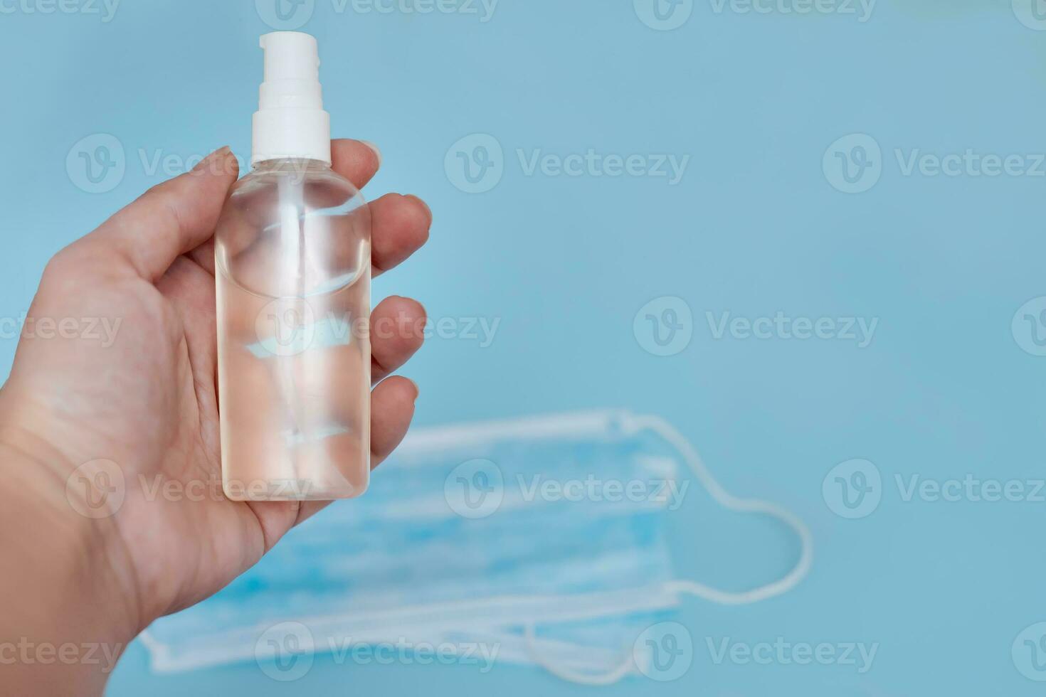 disinfectant in woman's hand on blue background with lying medical protective masks. Coronovirus, quarantine, epidemic, pandemic, cold, illness. Medicine concept and health. photo