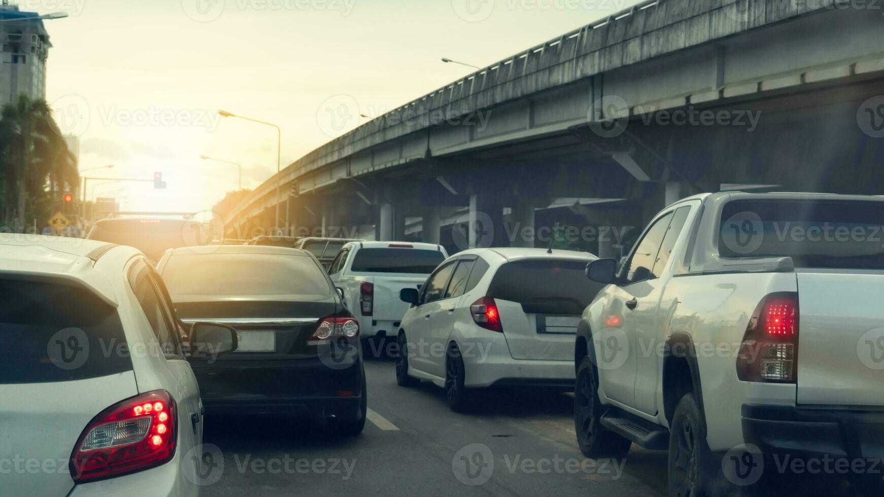 Rear side of white cars on the road with turn on brake light. Many cars stop on the road in the junction by traffic light control. Beside with level crossing made of concrete. Background of city. photo