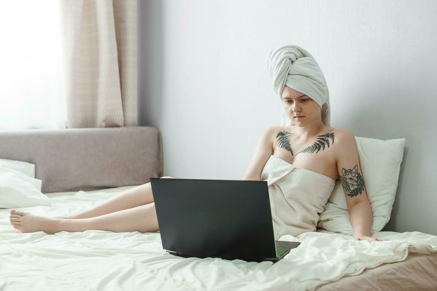 Tver, Russia-august 2, 2021. A tattooed woman after a shower is lying on the couch with a laptop. photo