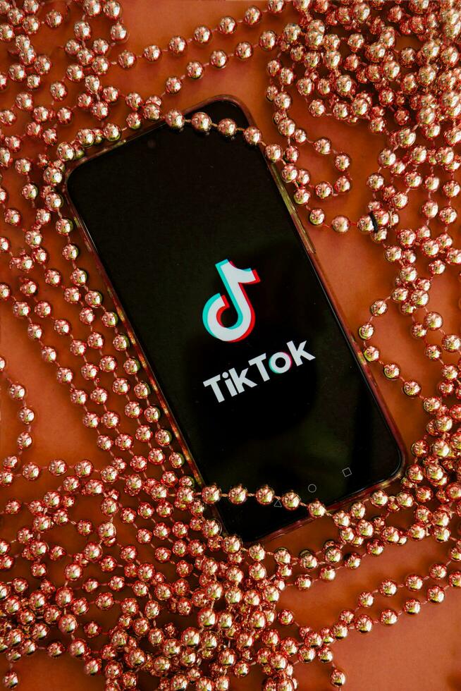 Tver, Russia - September 19, 2020. Tiktok app on your smartphone screen and Christmas beads on brown background. TikTok is a popular video sharing social network owned by ByteDance. photo